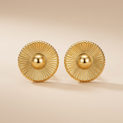 Paire de boucles d'oreilles puces dorées motif soleil, photo studio sur fond beige