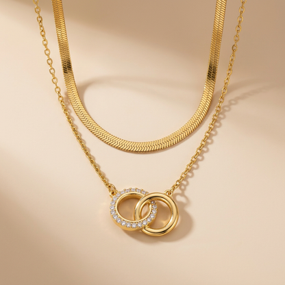 Collier double chaîne doré avec pendentif cercles entrelacés et cristaux, photo studio sur fond beige