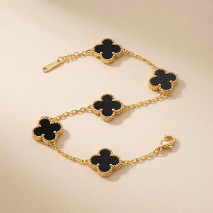 Bracelet doré à trèfles noirs posé sur fond beige, photo studio