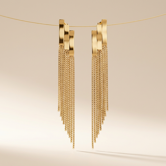Paire de boucles d'oreilles dorées pendantes à franges de chaînettes, photo studio sur fond beige
